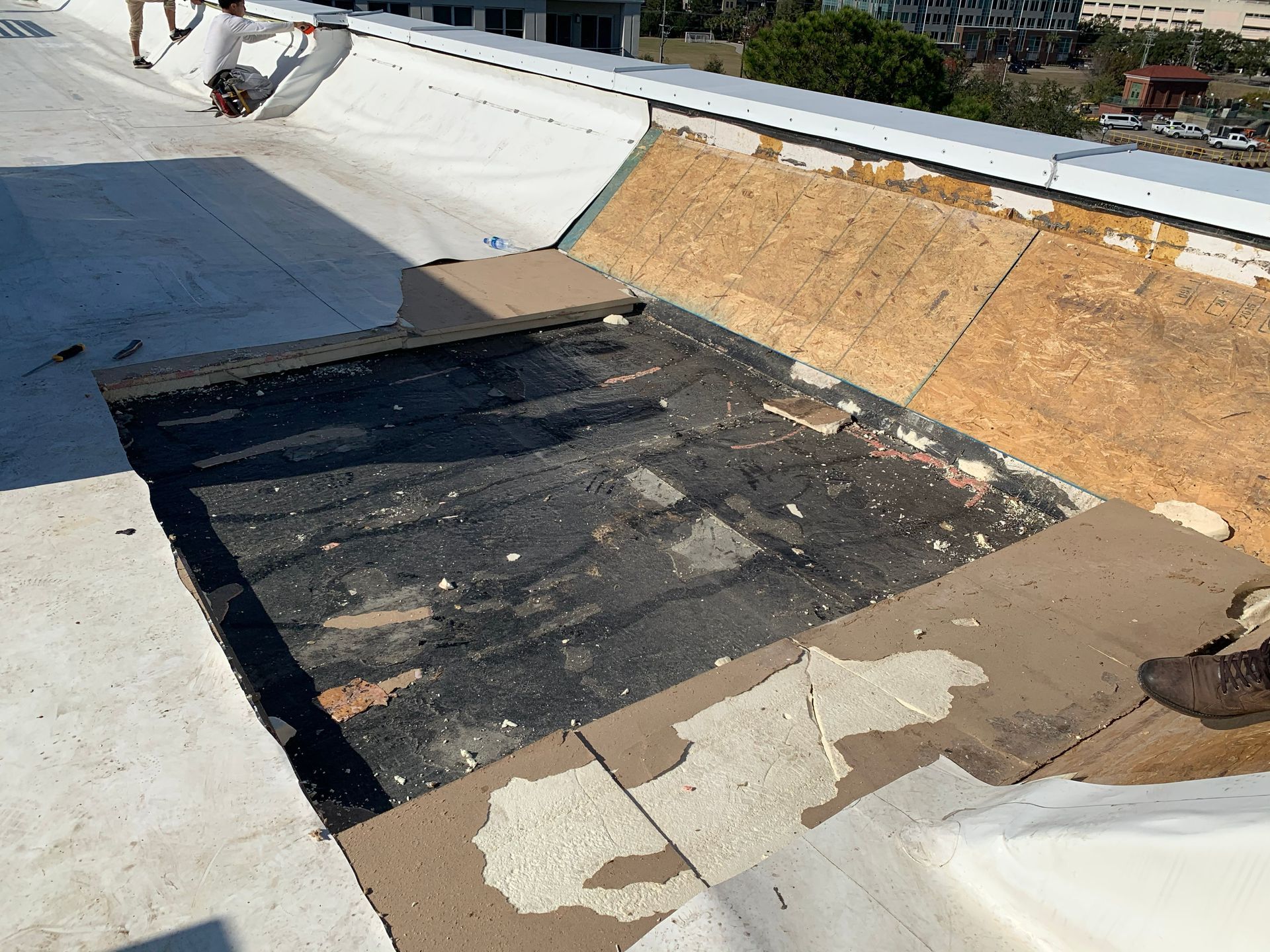 Roof repair: rectangular area cut out, exposing layers of materials, workers nearby.