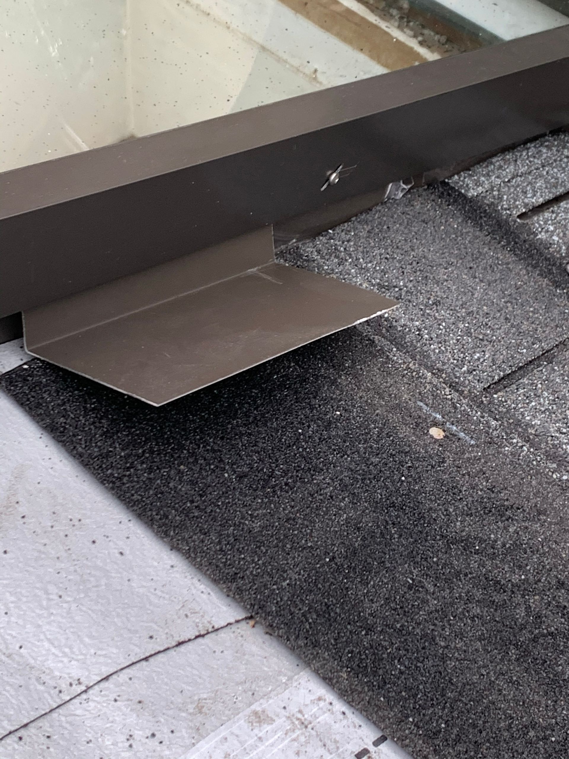 Metal flashing directs water away from a window frame, sitting atop asphalt shingles.