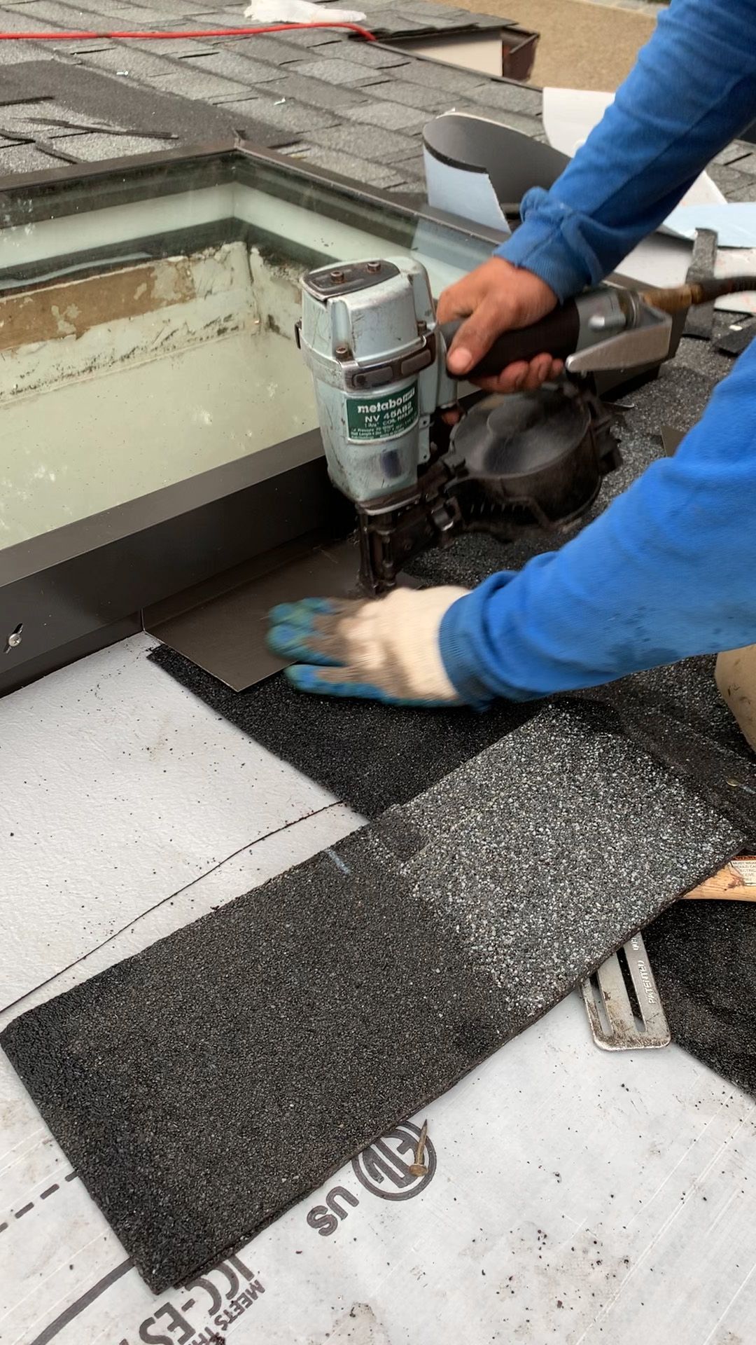 Roofer using a nail gun to install roofing shingles around a skylight.