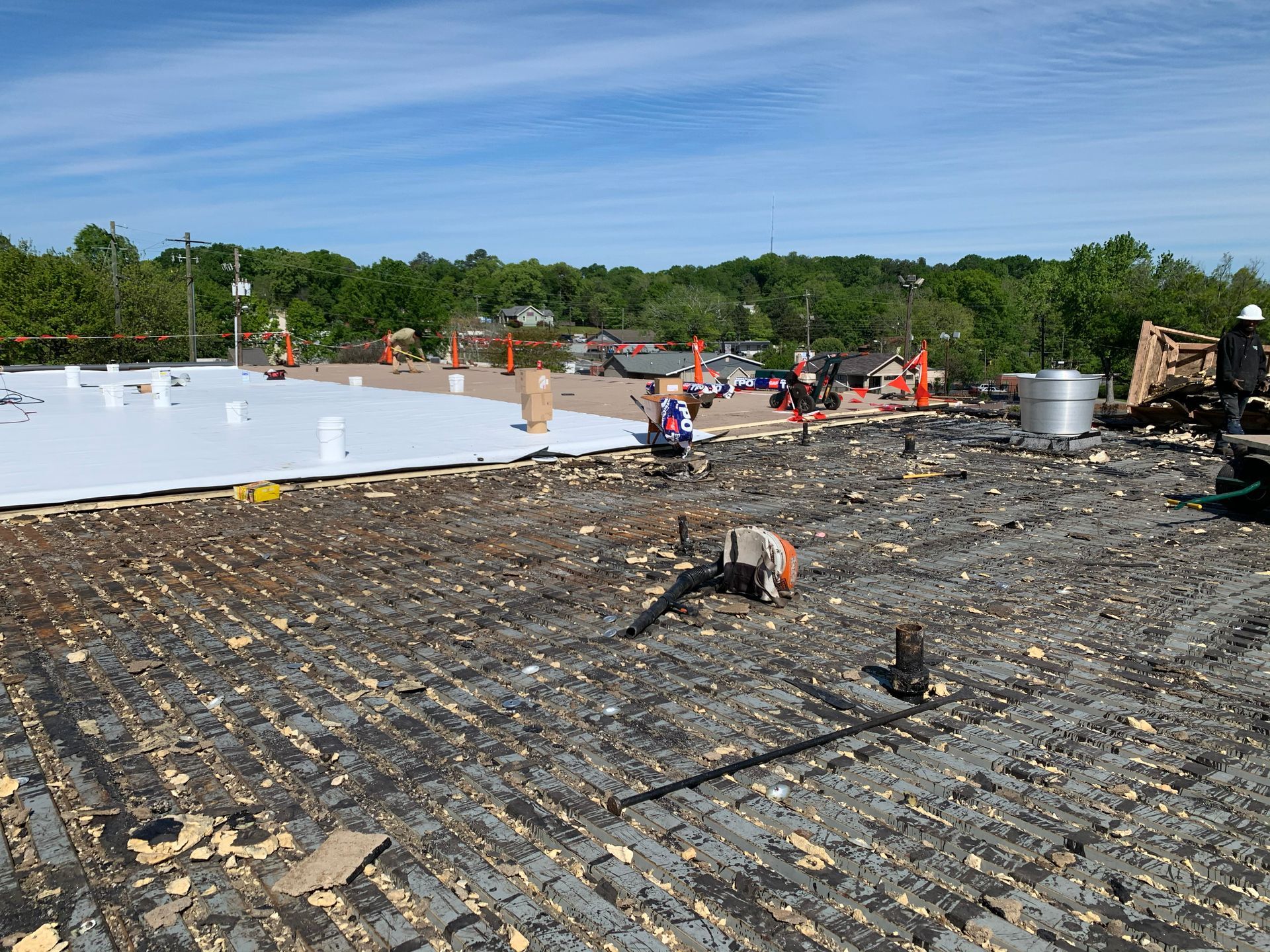 Roof repair on a commercial building; worn, exposed surface with new white membrane in progress, construction cones.