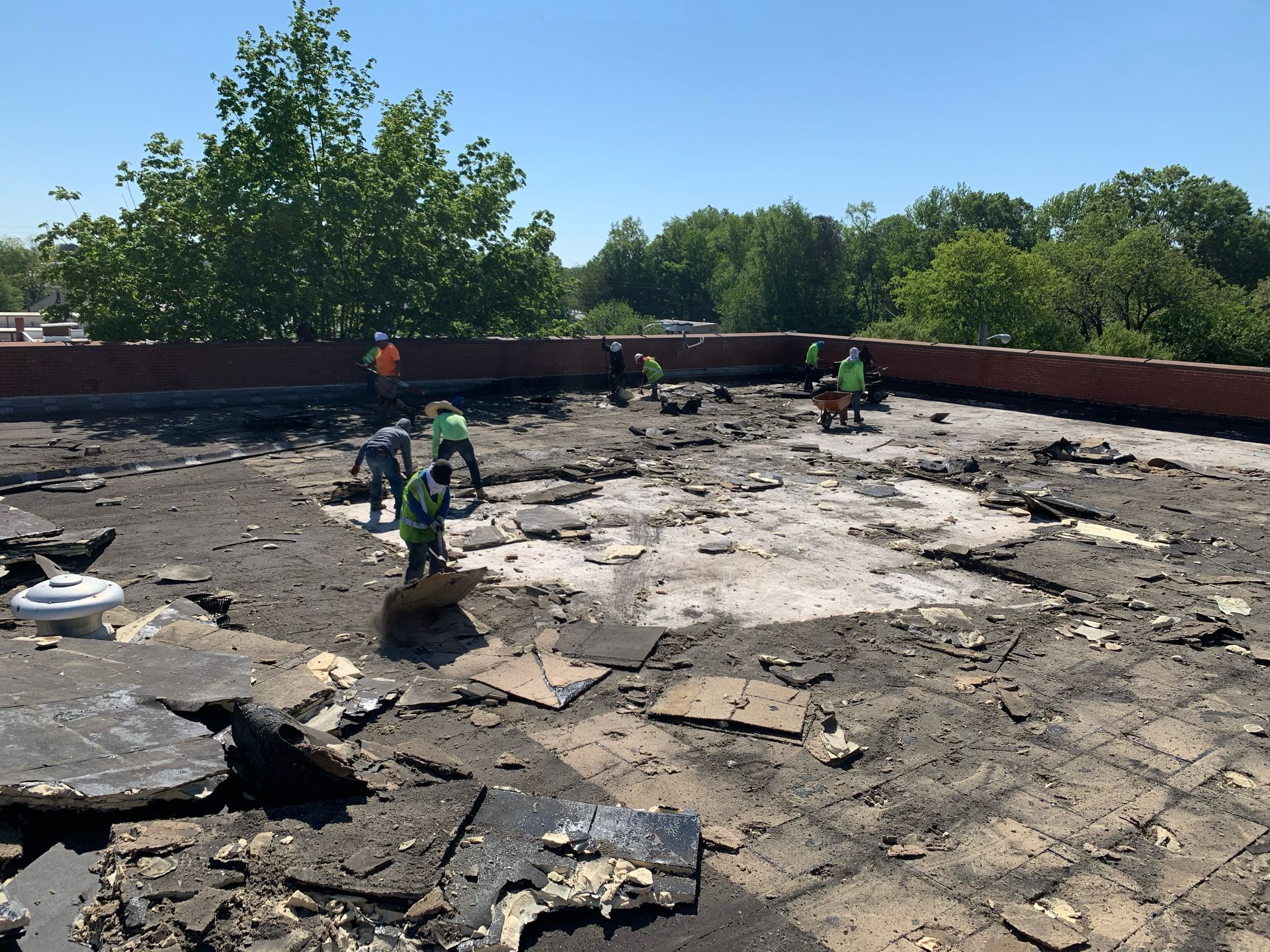 Roofing workers removing old roofing material on a flat roof under a blue sky.