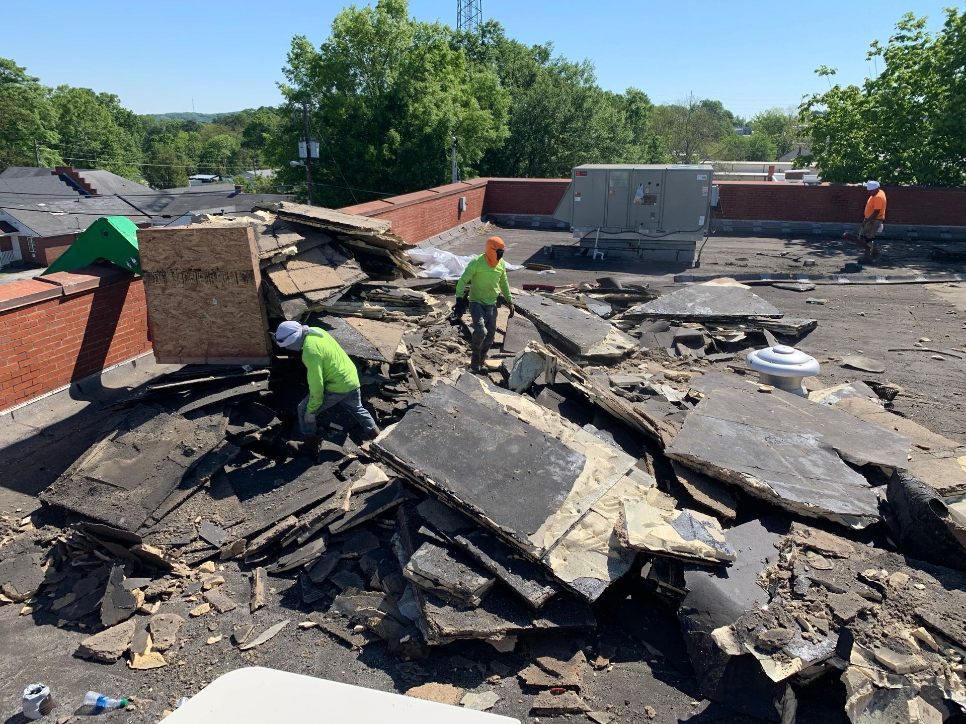Workers in hard hats tear up a roof, surrounded by debris.