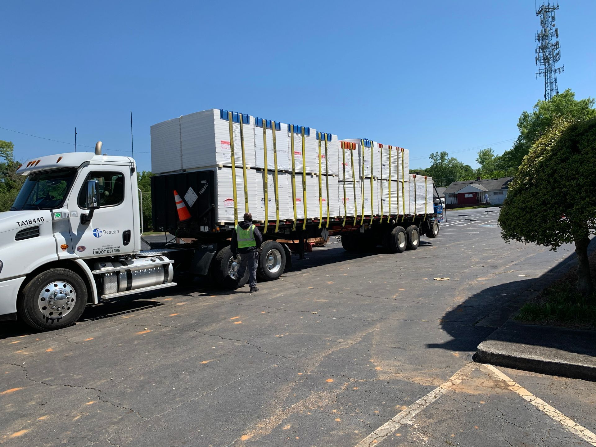 Truck with large load of white rectangular blocks, parked on asphalt. Man in safety vest stands near trailer.