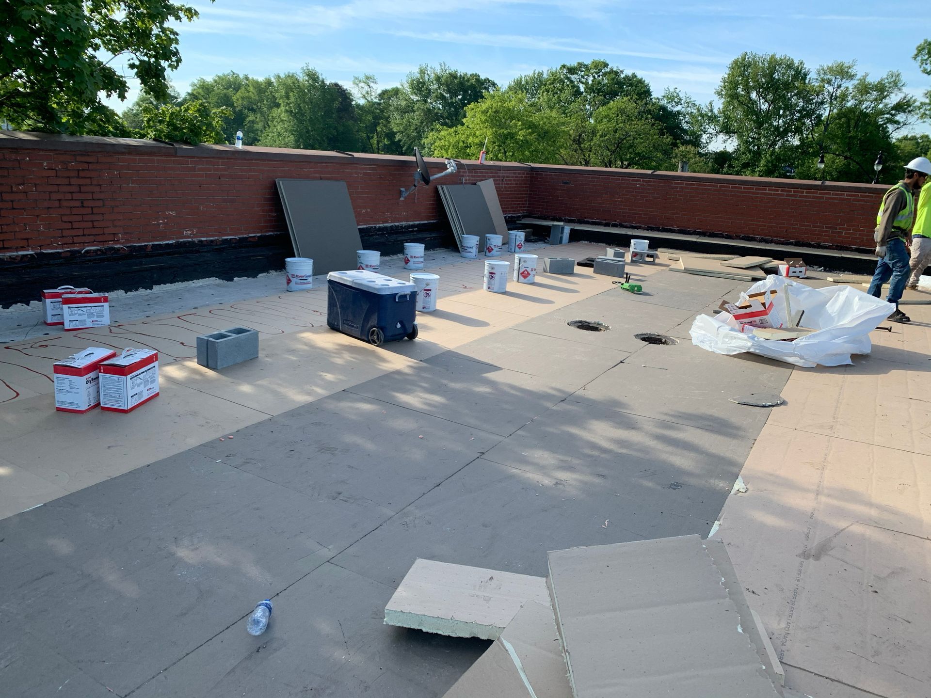 Workers on a flat roof, surrounded by supplies, installing roofing material on a sunny day.