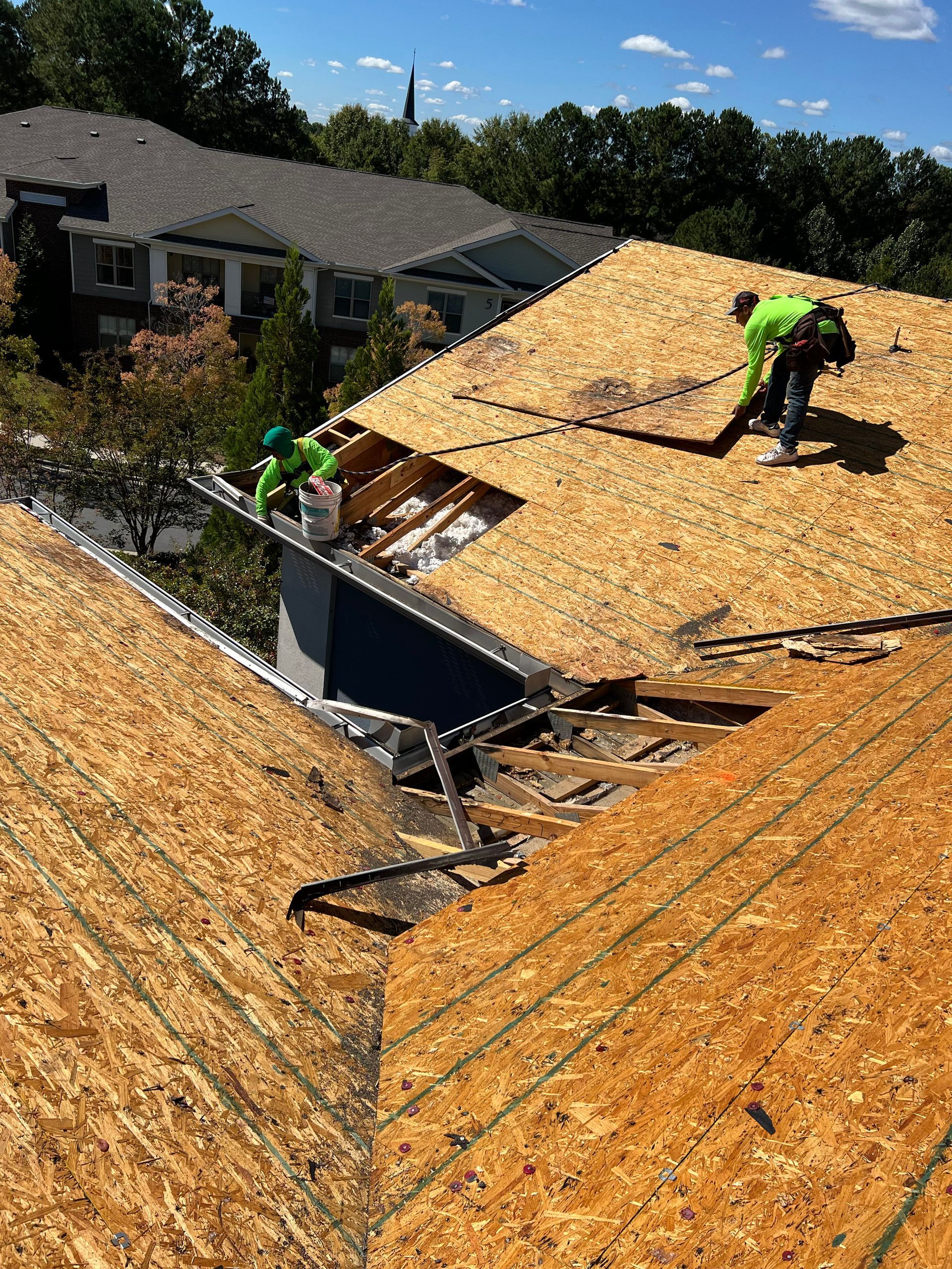 Roofers in green gear working on a roof, sunny day.