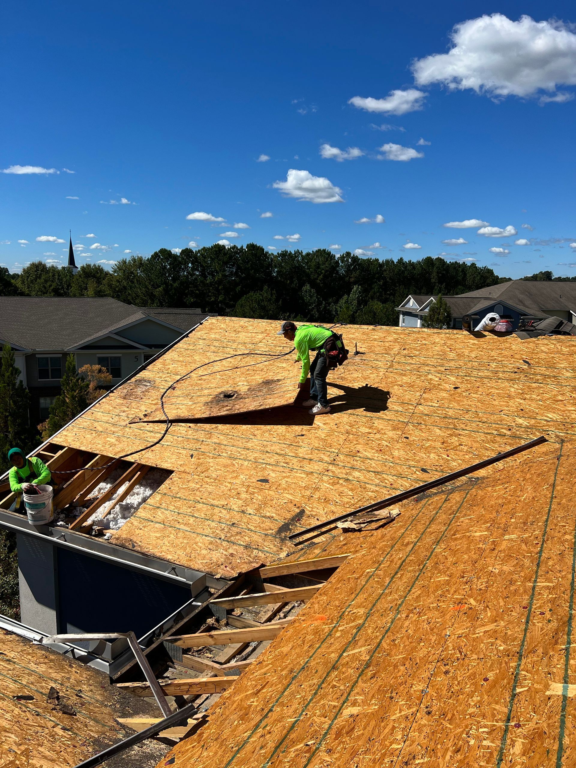 Roofers in neon green shirts working on a rooftop with clear blue sky in background.
