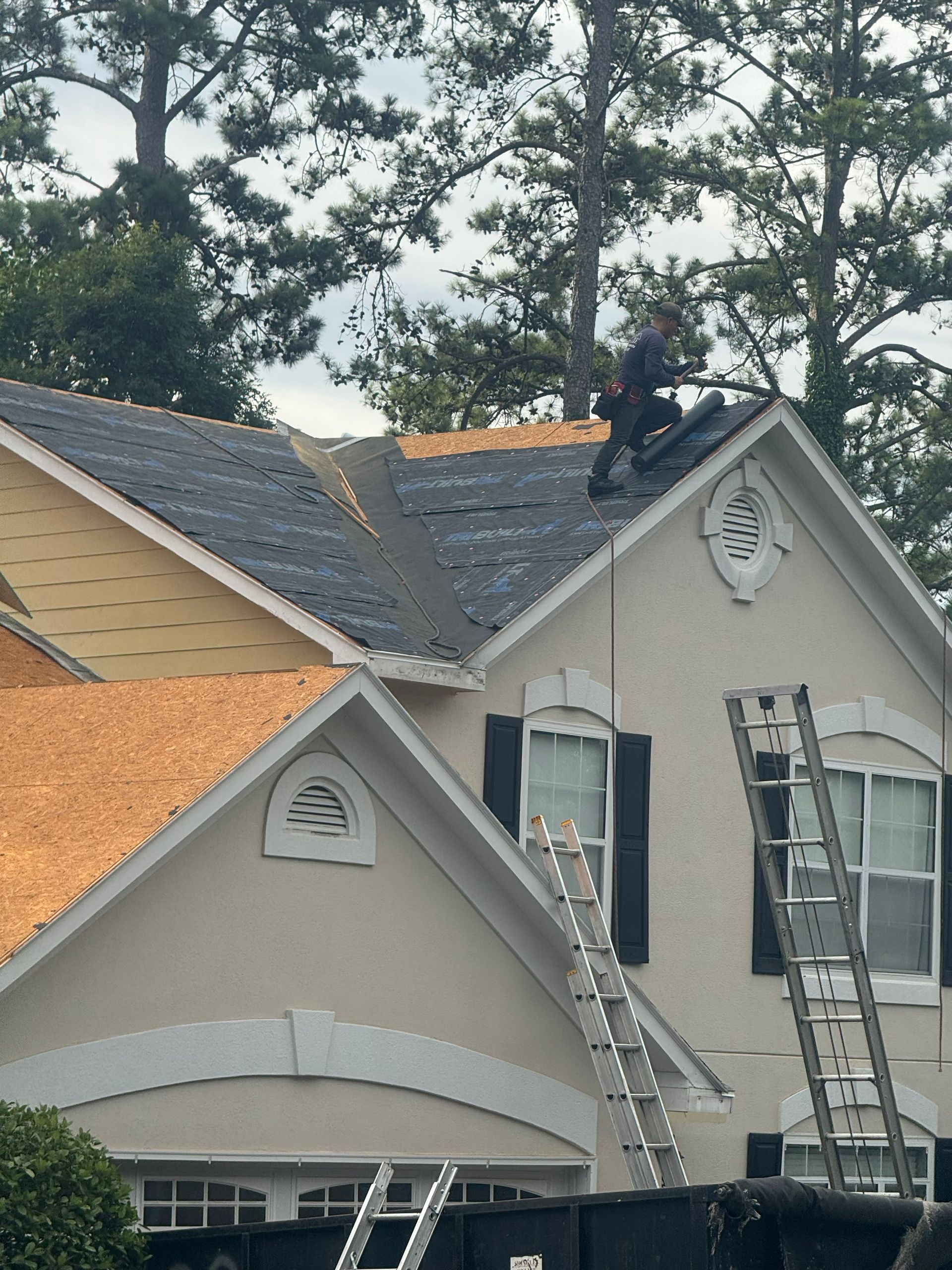 Roofer on a house roof. New roofing material being installed. Ladders are positioned on the house.