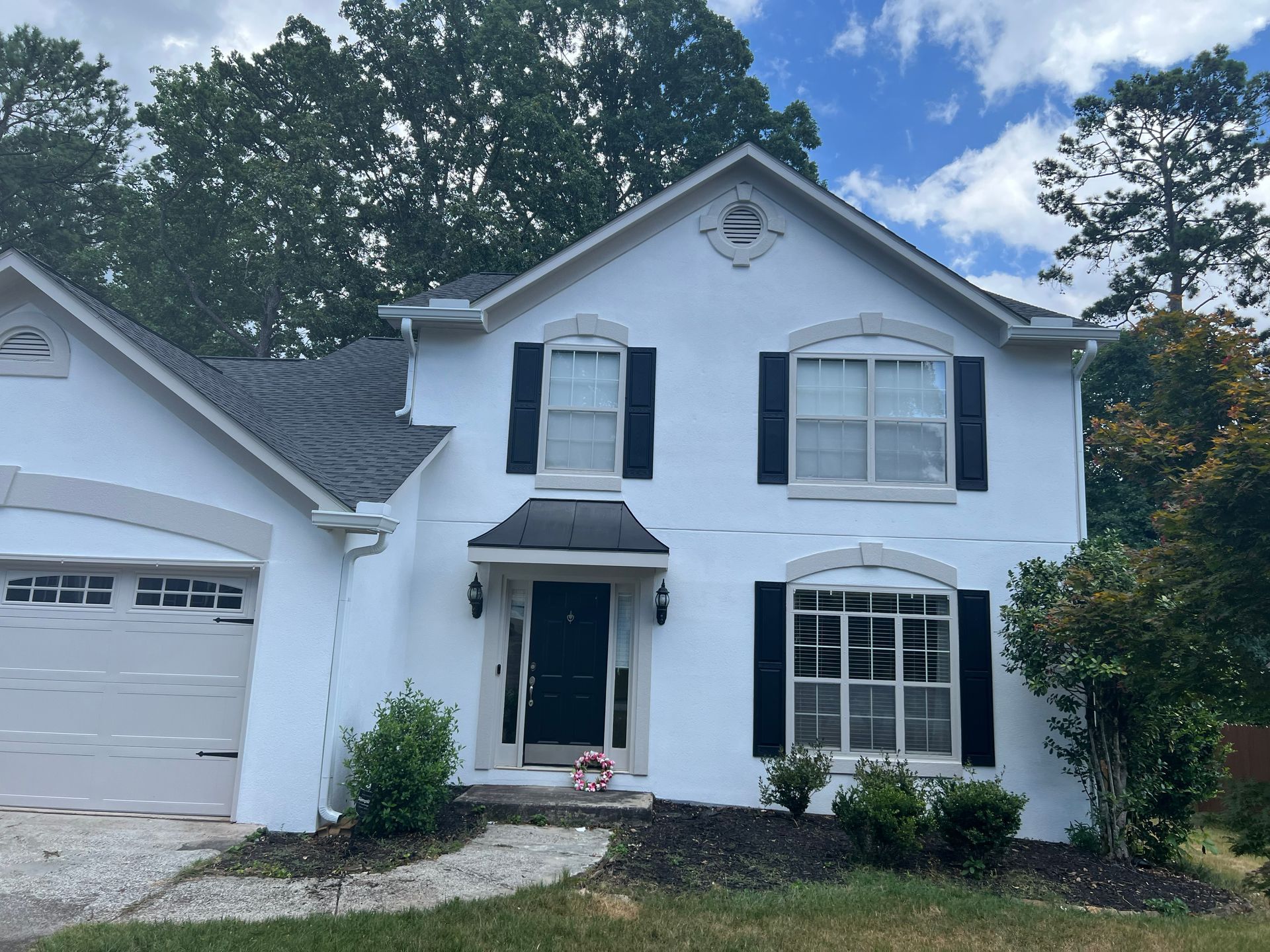 White house with black shutters, door, and gray roof, blue sky, and green trees.