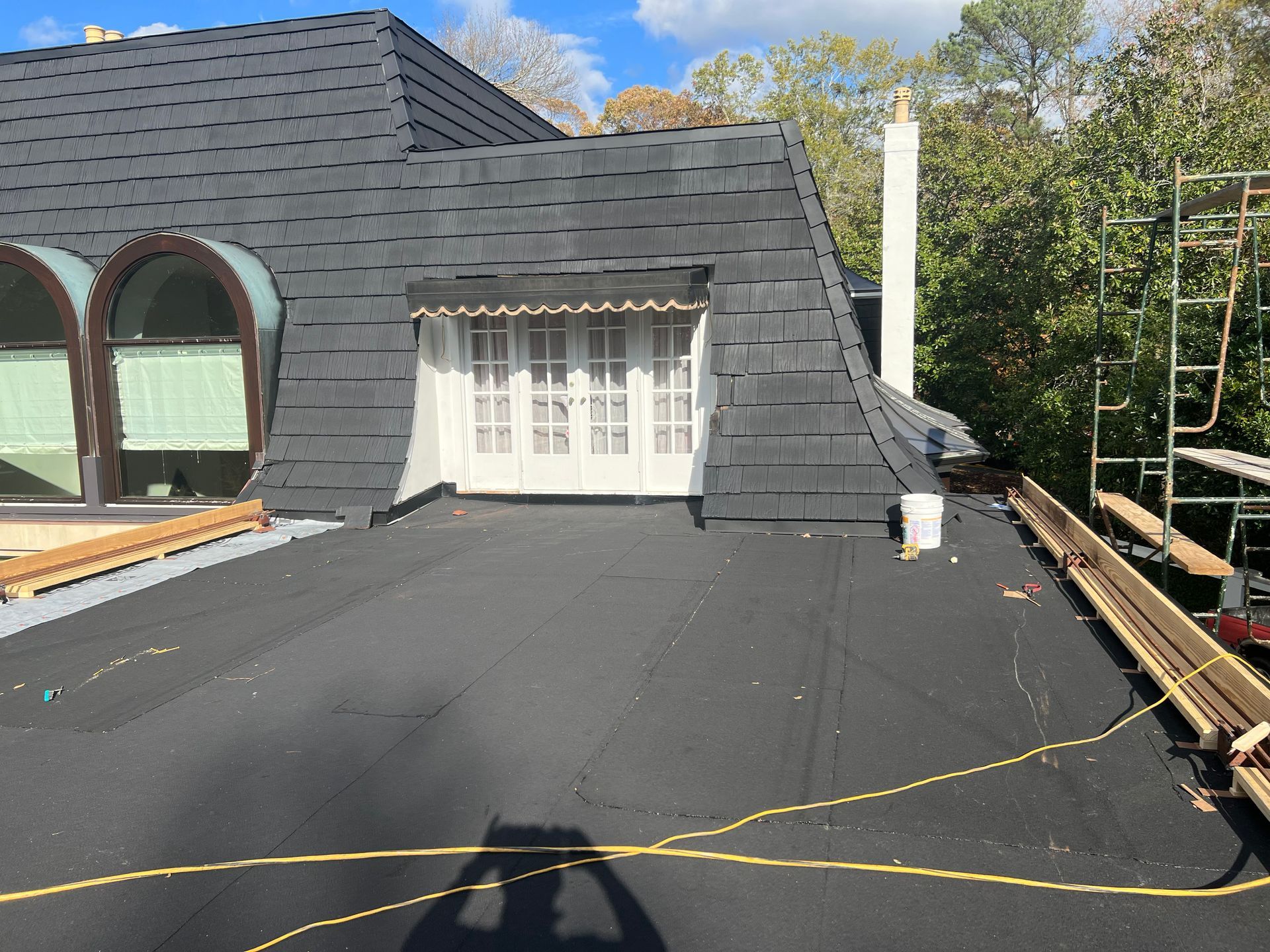 Black roof with a dormer and arched windows. A white chimney is visible. Scaffolding on the right.