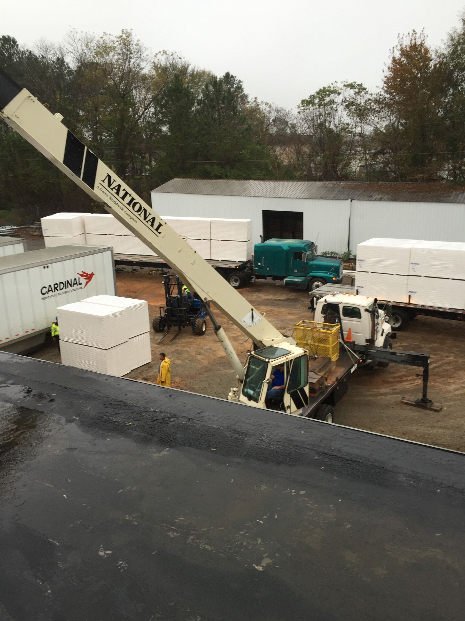 Crane unloading large white packages from trucks. Outdoors, overcast day.