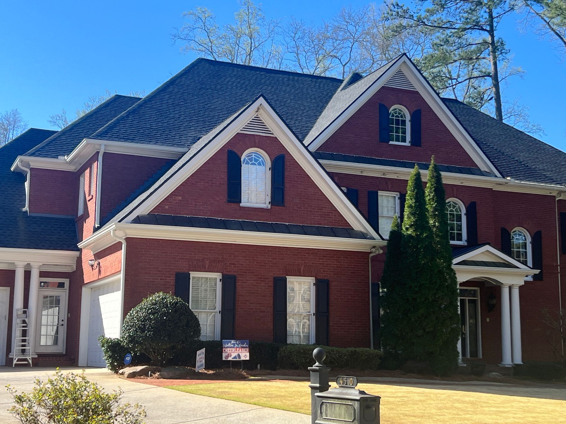 Red brick house with dark roof and white trim under a clear, blue sky.