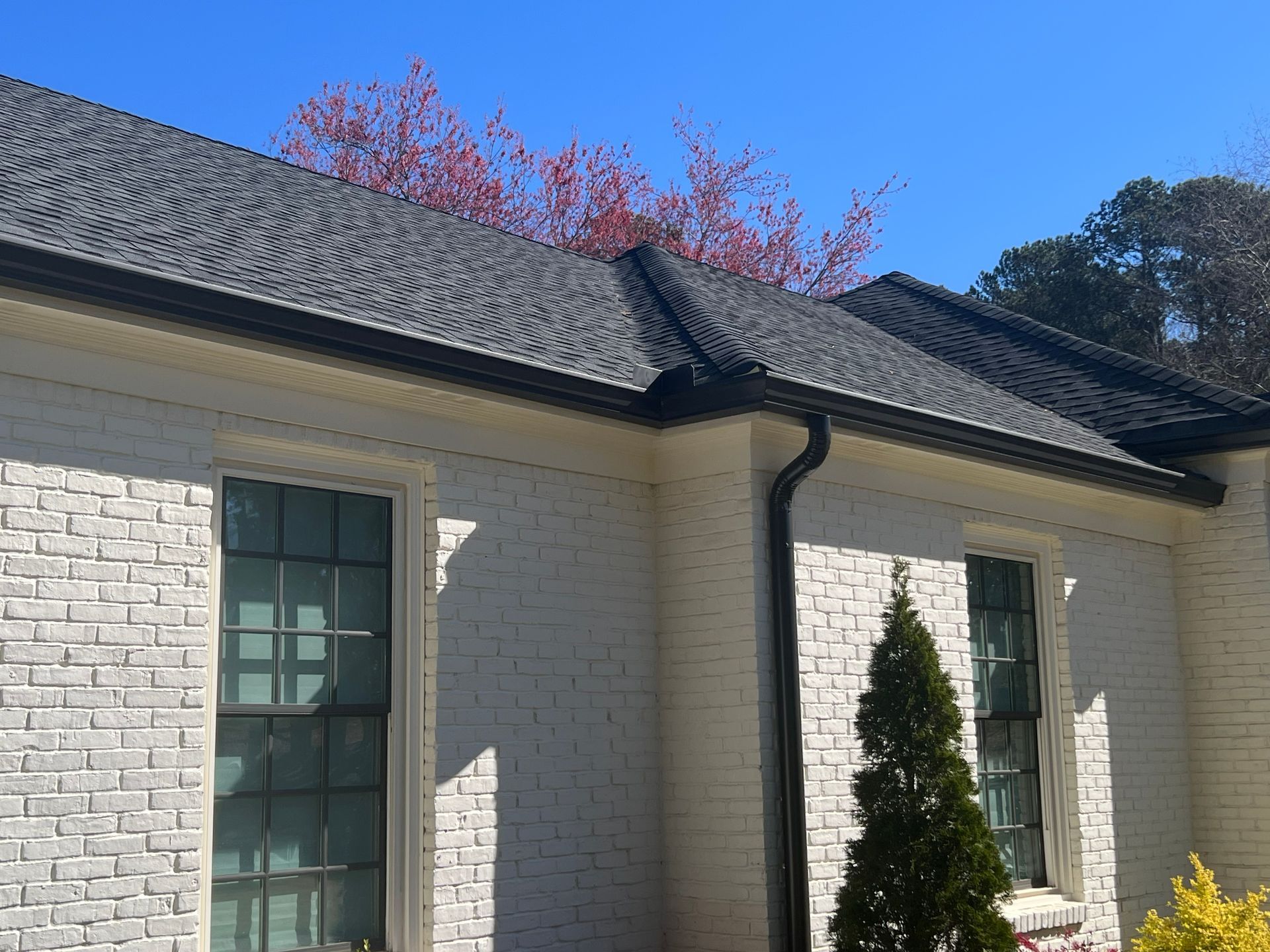 White brick house with black roof and gutters, blue sky.