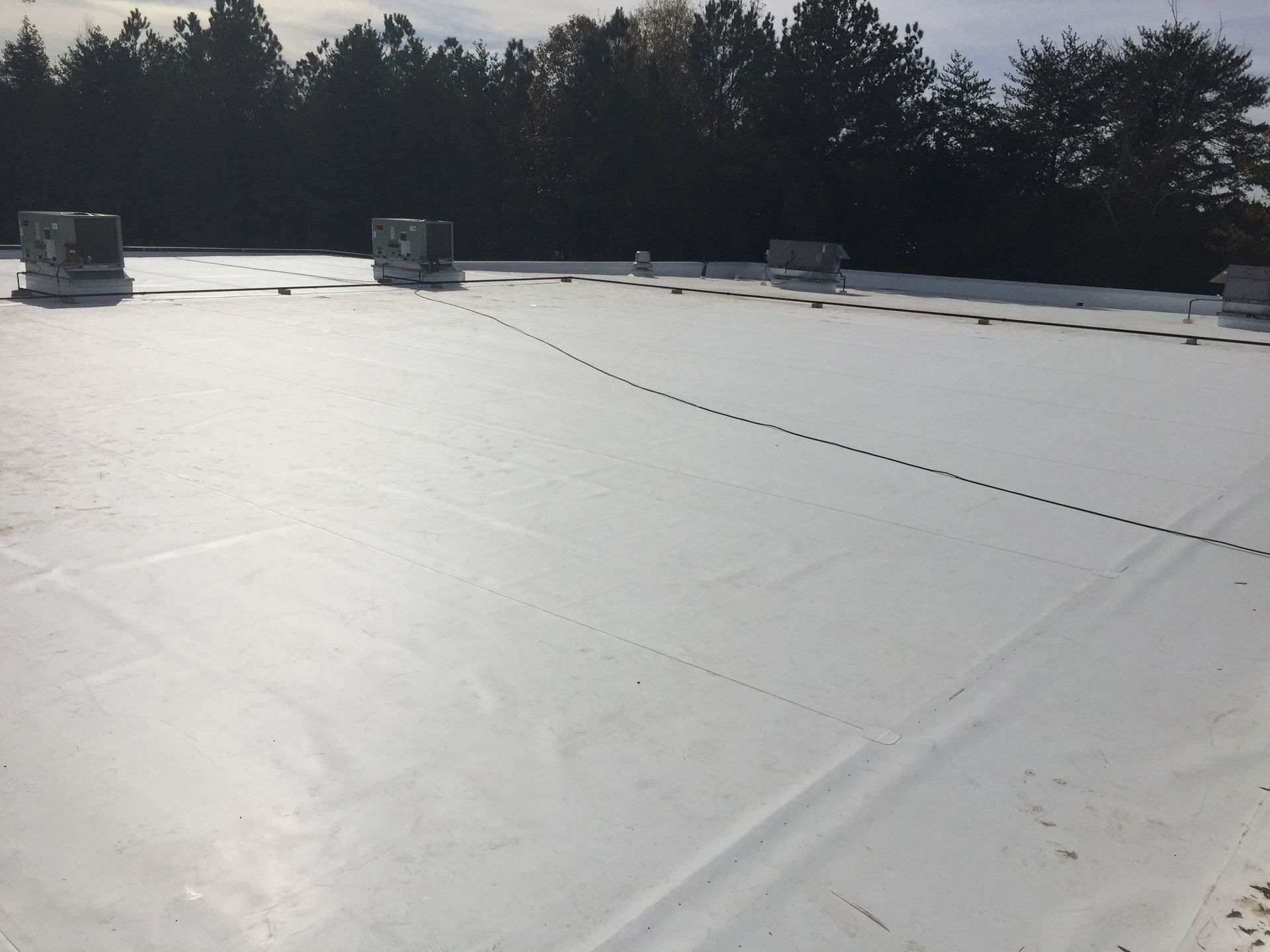 White commercial flat roof with HVAC units, treetops in background.