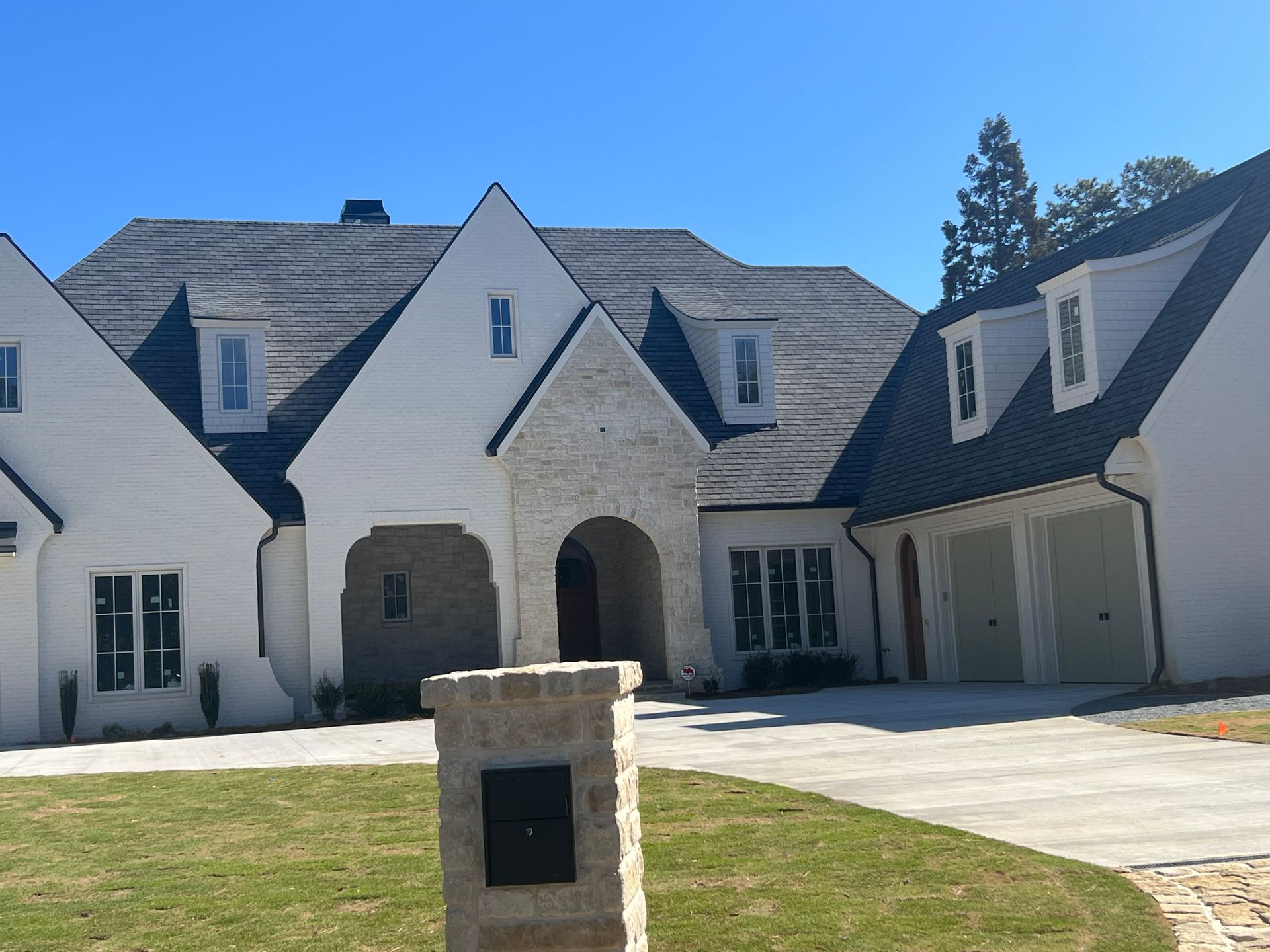 White and stone facade home with dark roof, dormer windows, and attached light green garage doors.
