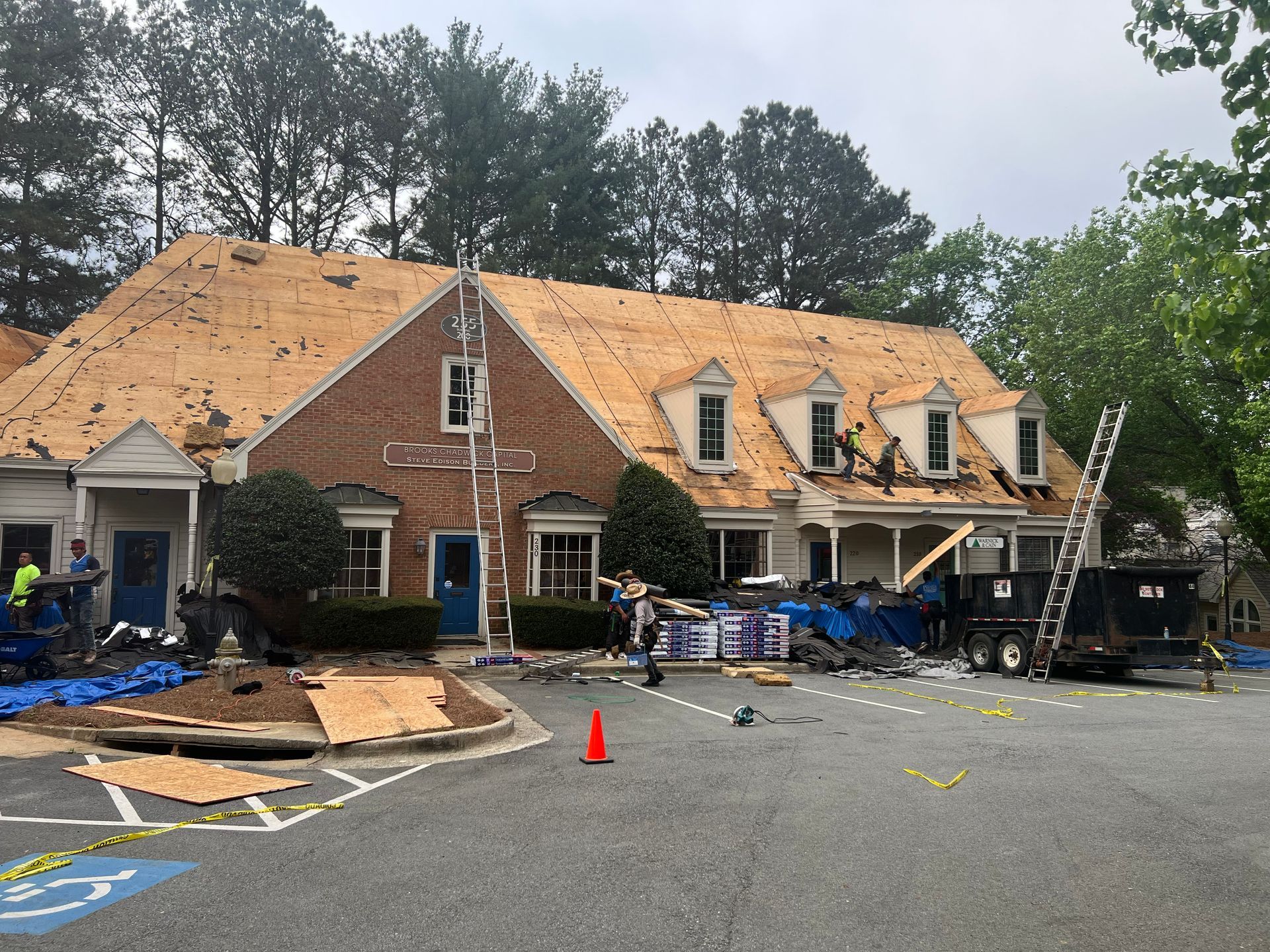 Building with a damaged roof undergoing repairs; workers and materials on site.