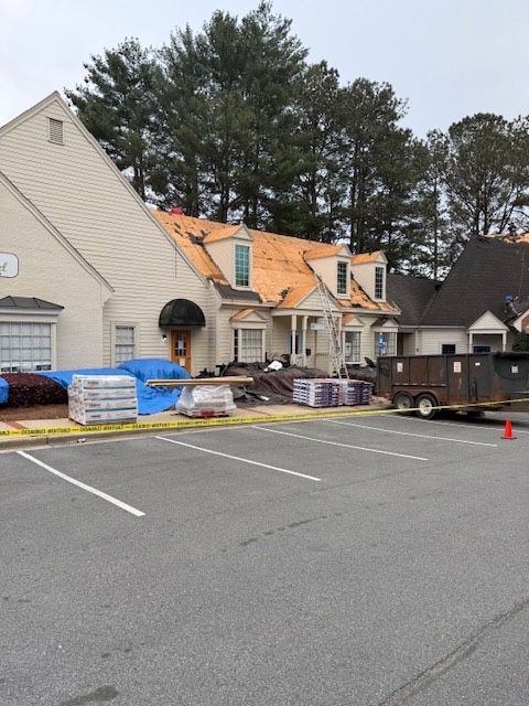 Roofing work in progress on a light-colored building. Debris, materials, and a dumpster are present.