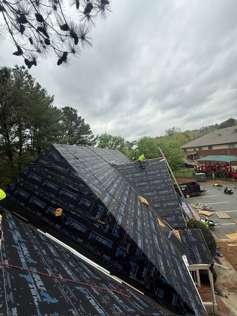 Roofers installing shingles on a roof, under an overcast sky.