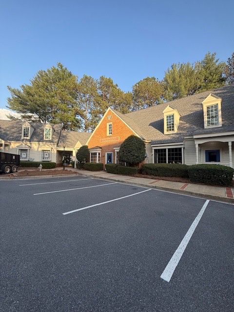 Buildings with asphalt parking lot; red brick and beige exteriors, topped with a blue sky and trees.