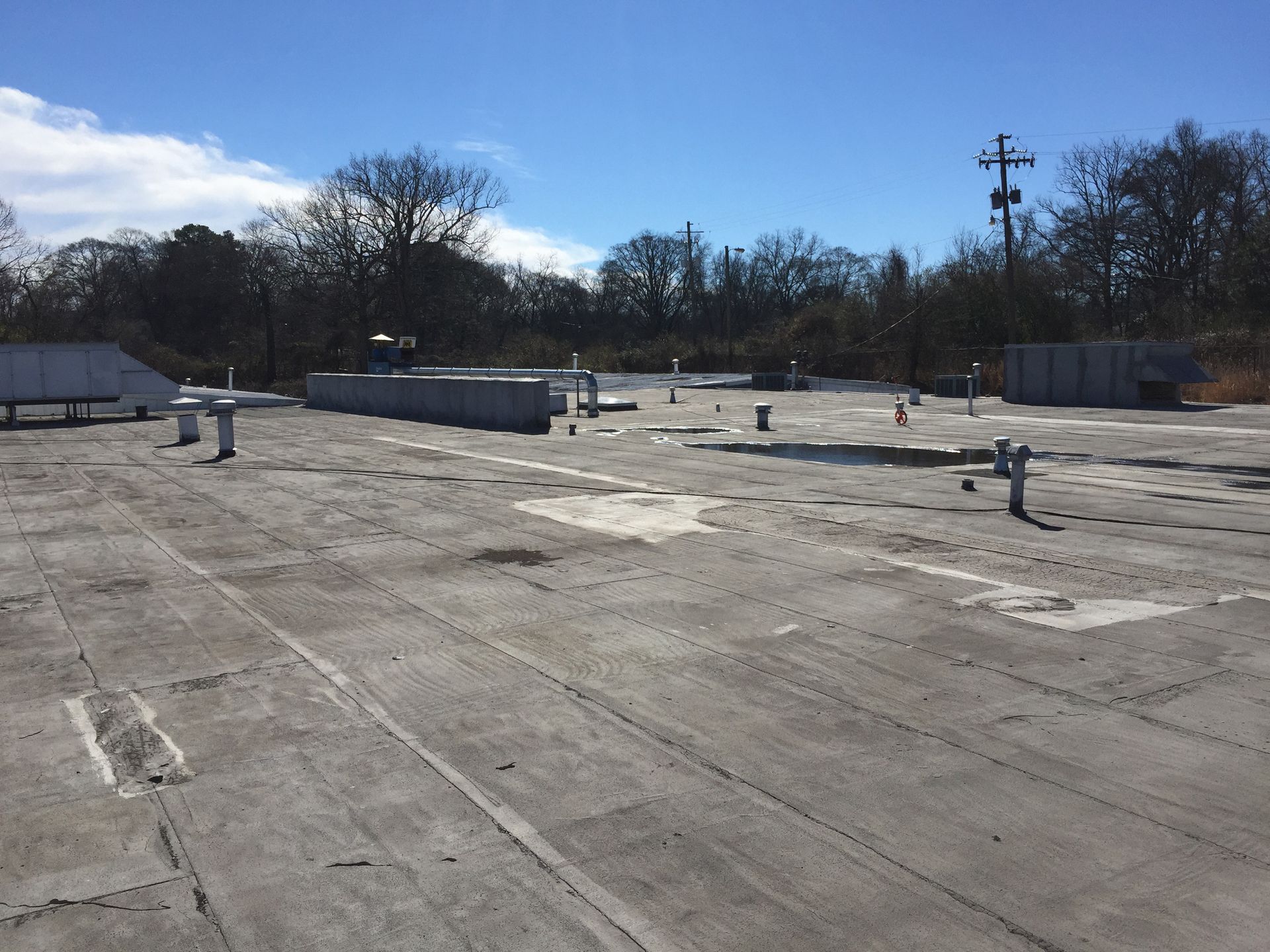 Flat, light gray commercial rooftop with vents and equipment against a clear, sunny sky.