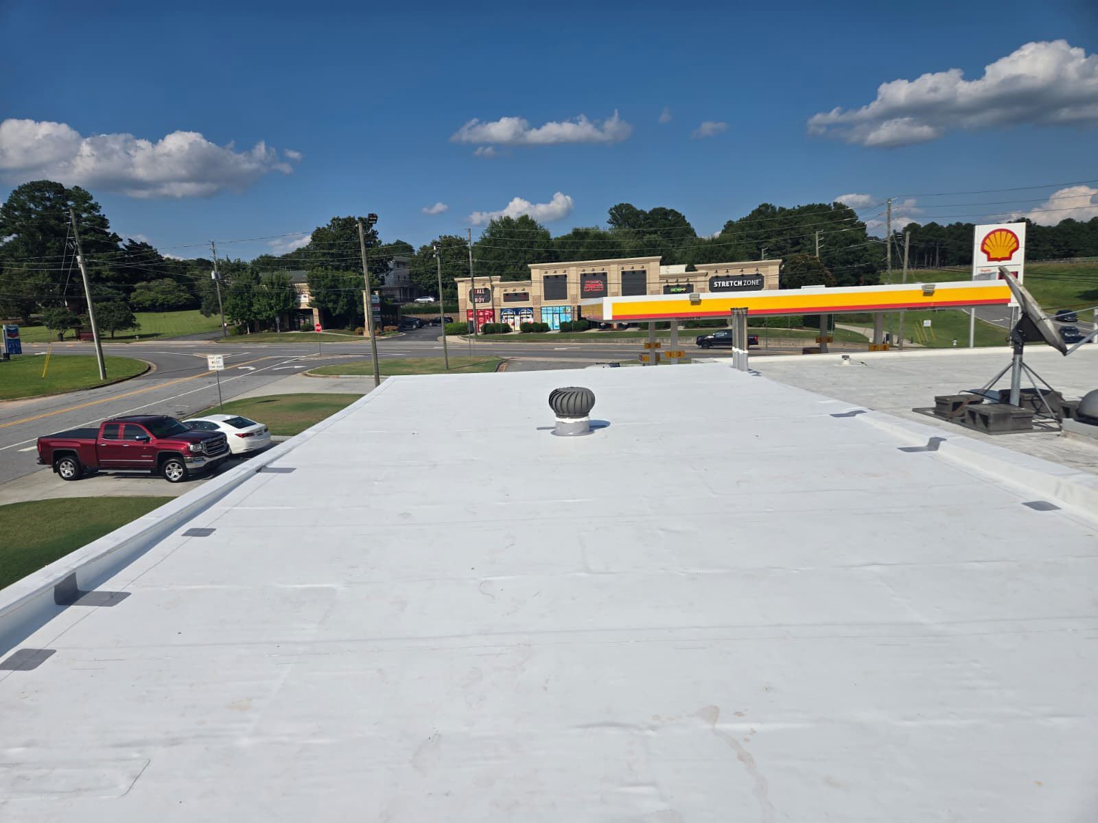View of a white commercial roof with a Shell gas station and surrounding businesses on a sunny day.