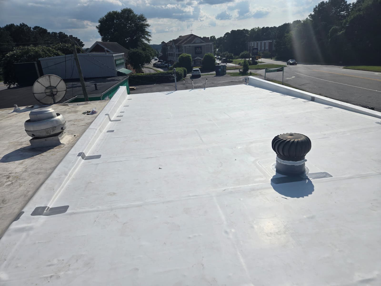 White flat commercial roof with vents and road in background.