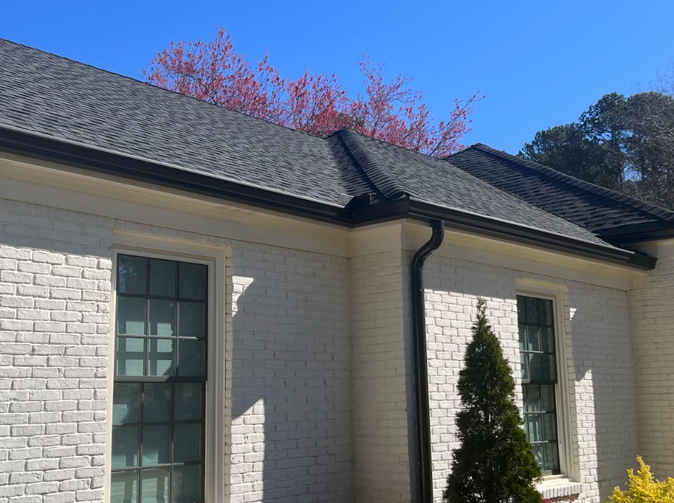 White brick house with dark roof, gutters, and windows against a blue sky.