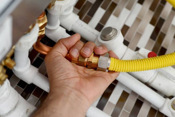 Hand holding a yellow gas line connected to brass fittings and white pipes.