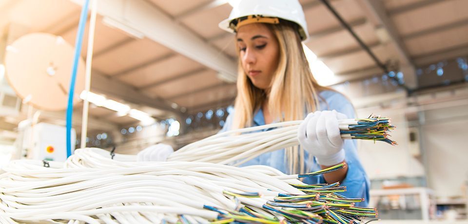 A woman is working in a factory holding a bunch of custom cable assemblies.