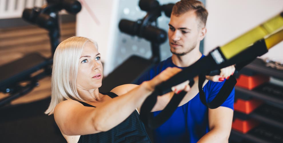 A man and a woman are doing trx exercises in a gym.