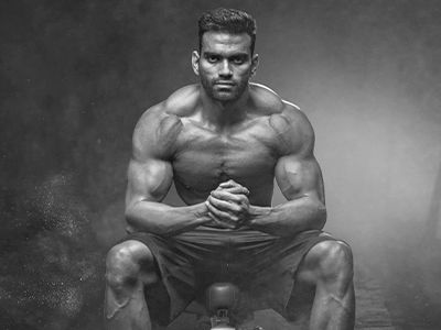 A shirtless man is squatting on a barbell in a black and white photo.