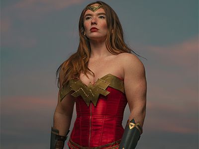 A woman in a wonder woman costume is standing in front of a cloudy sky.