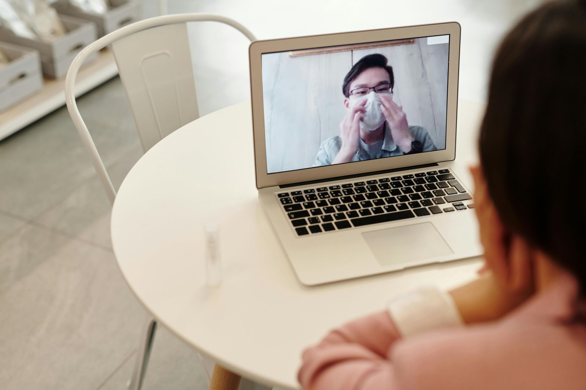 Person on laptop video call, demonstrating how to put on a face mask.