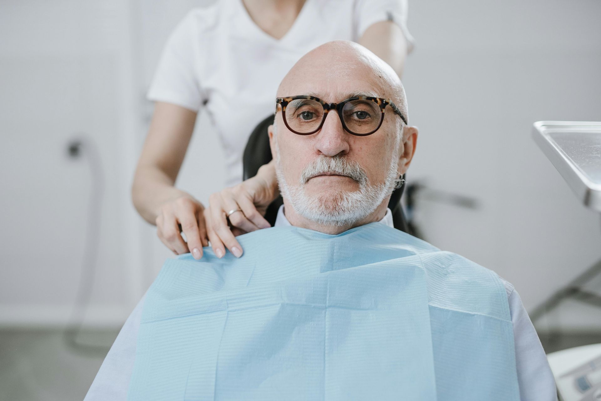 Man in dental chair, bib on, getting shoulder adjustment from dental assistant.