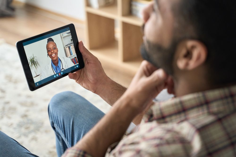 Man on couch having a telehealth appointment on a tablet with a doctor.