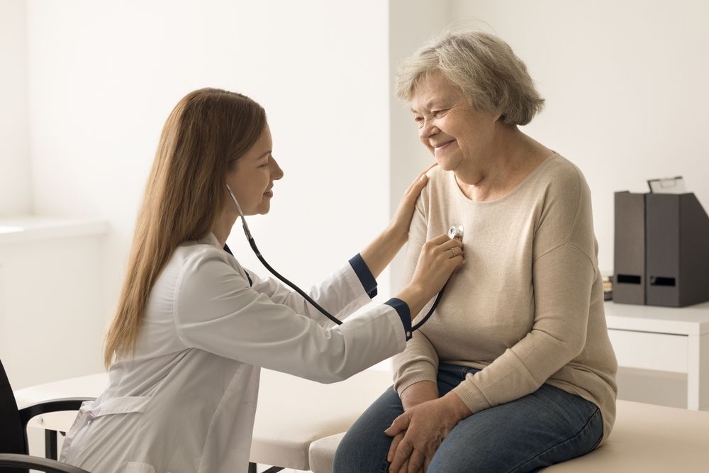 Doctor listening to patient's heart with a stethoscope in a bright medical office.