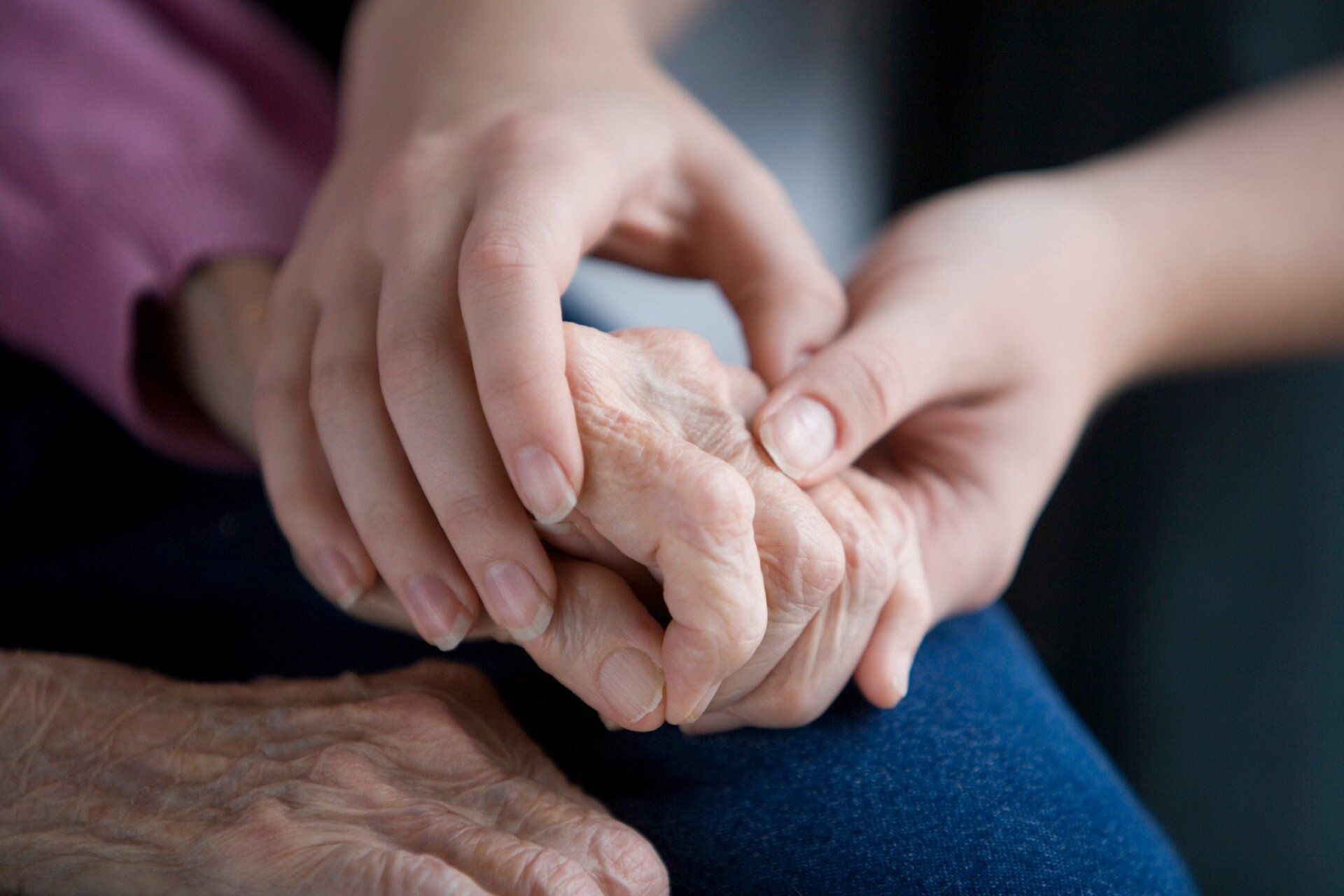 Young hand gently holding the wrinkled hand of an elderly person, showing comfort and support.