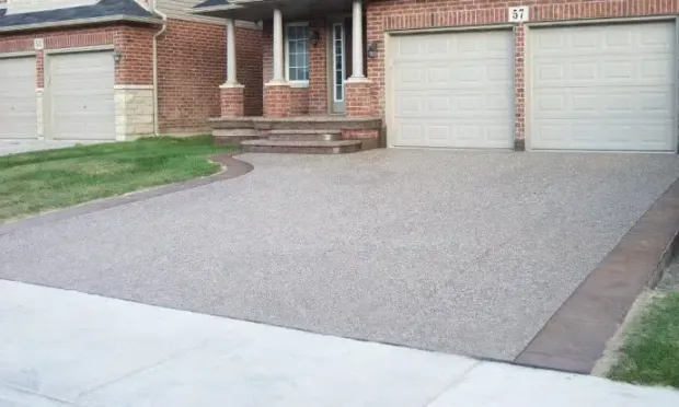 A driveway leading to a brick house with two garage doors.