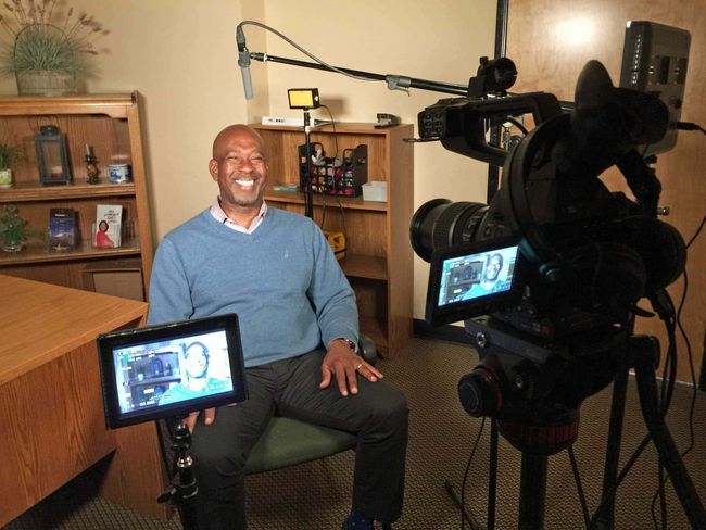 A man is sitting in front of a camera and smiling