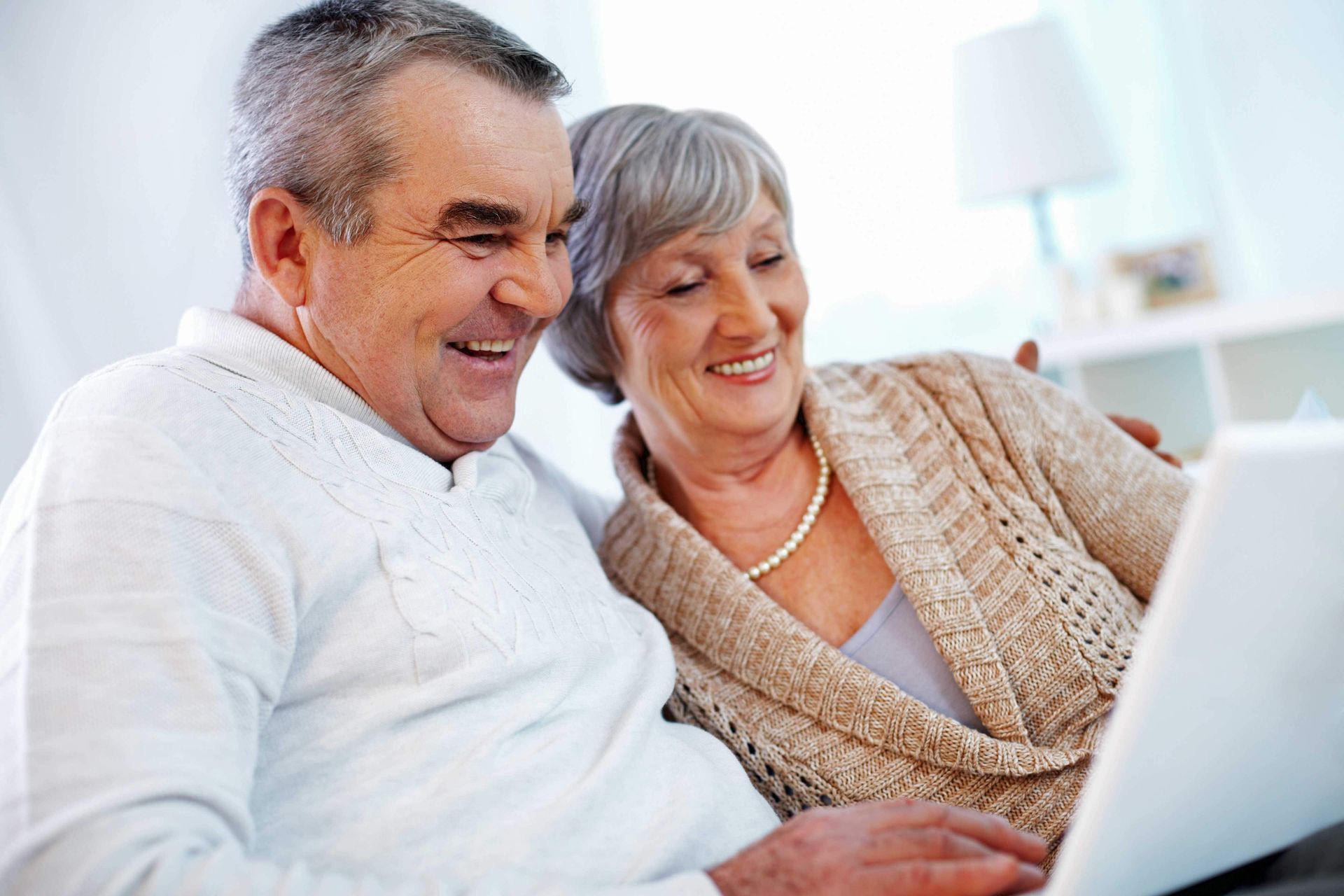An elderly couple is sitting on a couch looking at a laptop computer.
