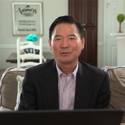 A man in a suit is sitting on a couch in front of a laptop