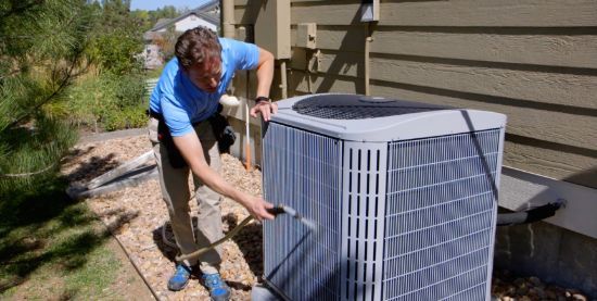 A man is cleaning an air conditioner outside of a house.