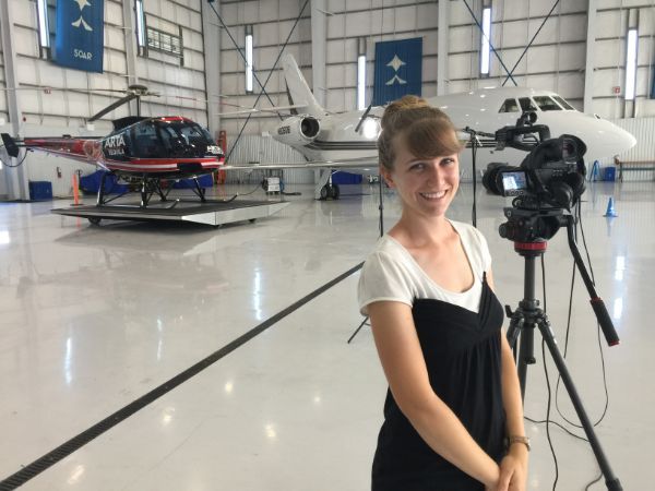 A woman stands in front of a camera in an airplane hangar