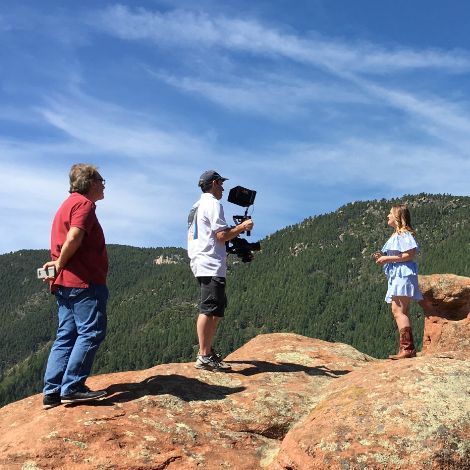 A group of people are standing on top of a rocky hill talking to each other.