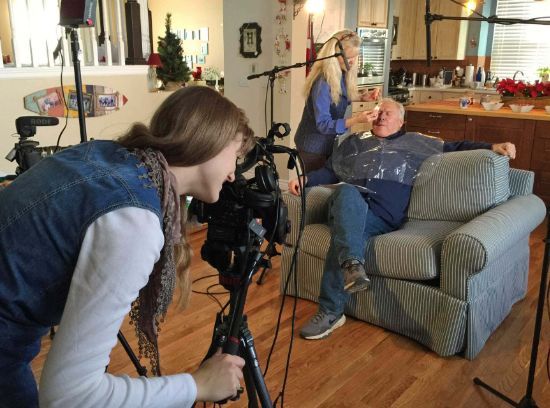 A woman is taking a picture of a man sitting in a chair