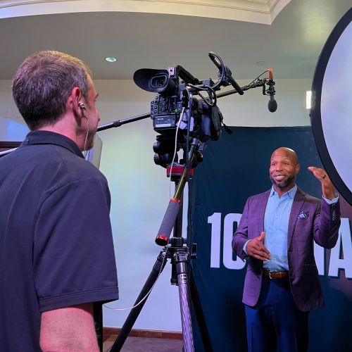 A man in a suit is talking to another man in front of a camera.