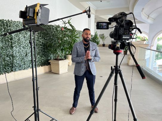 A man is standing in front of a camera on a tripod.