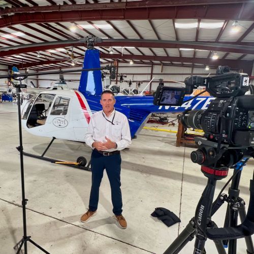 A man is standing in front of a helicopter in a hangar.
