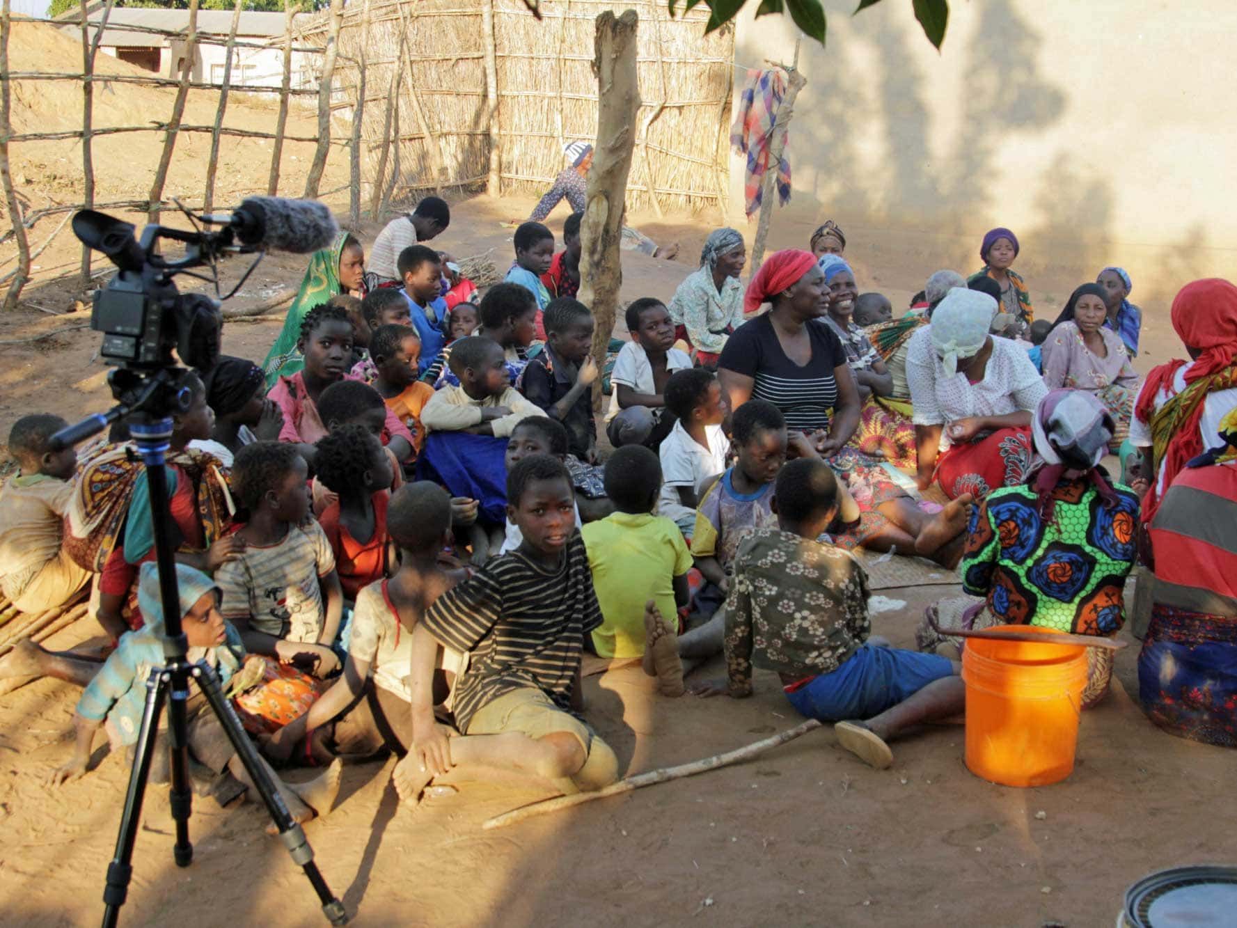 A group of people are sitting on the ground in front of a camera
