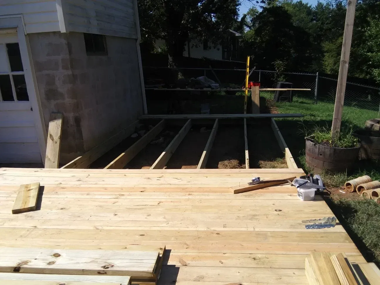A partially built wooden deck in a yard next to a cinder block building, showing the framing and decking.