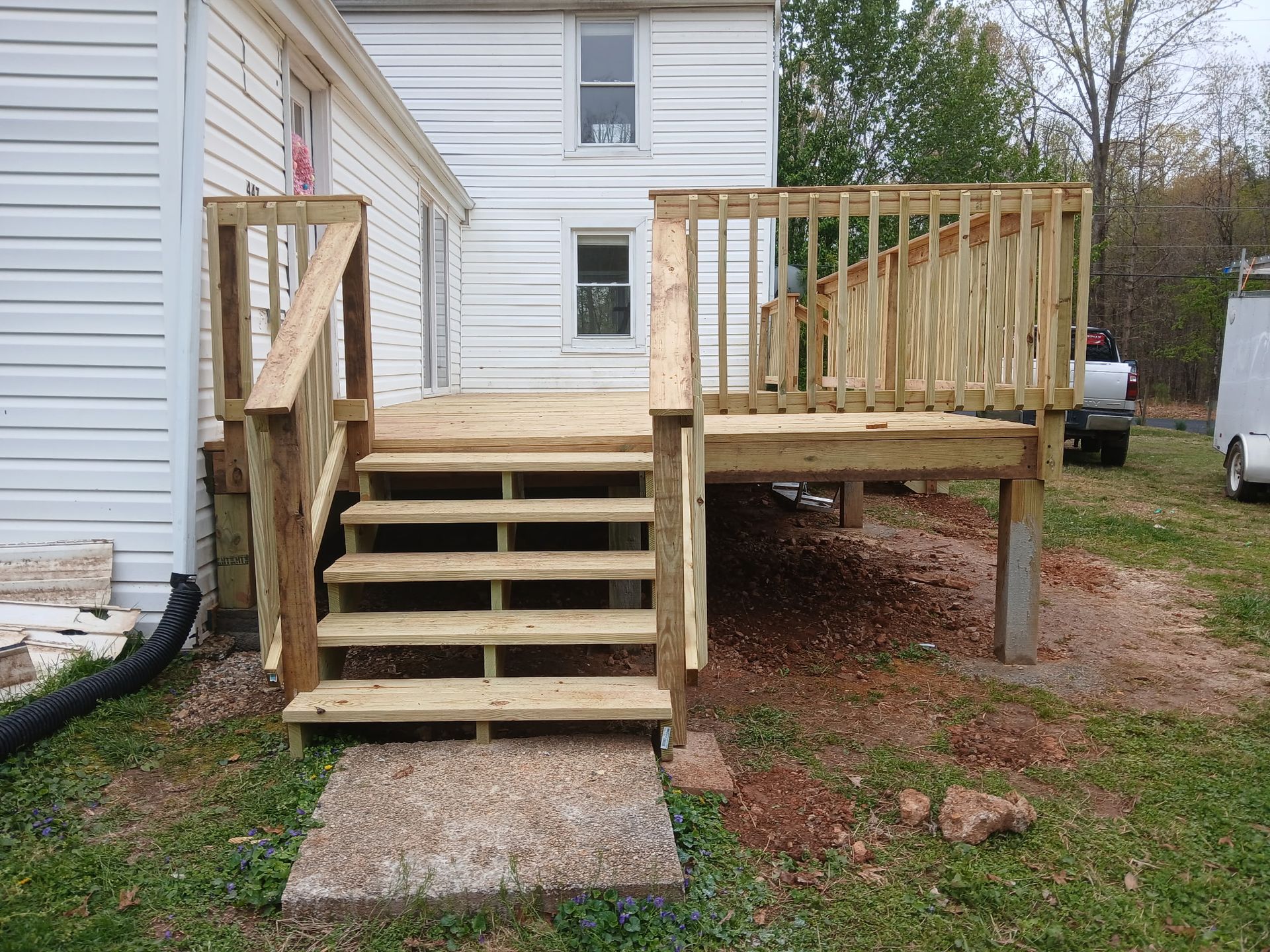 Wooden deck with stairs attached to a white house; steps lead to the yard.